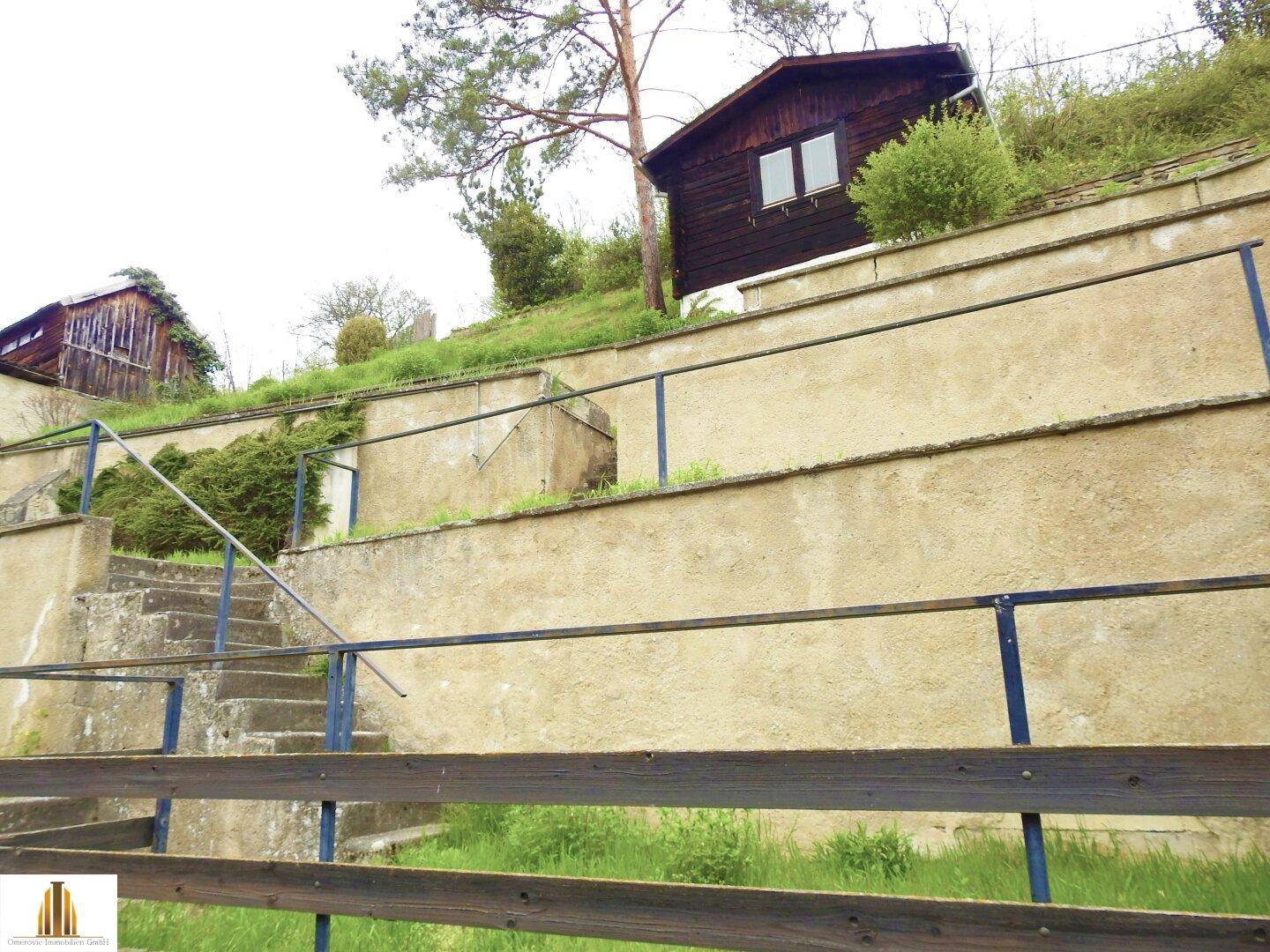 Terrassierter Gartenbereich mit Treppen und kleinen Gebäuden am Hang.