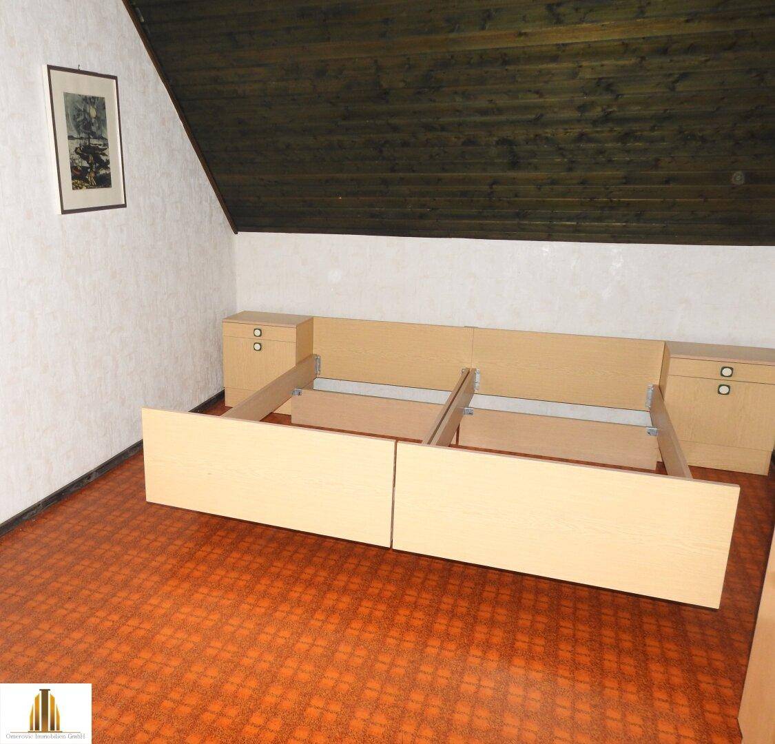 Schlafzimmer im Dachgeschoss mit schrägen Wänden, Holzboden und Bettrahmen.