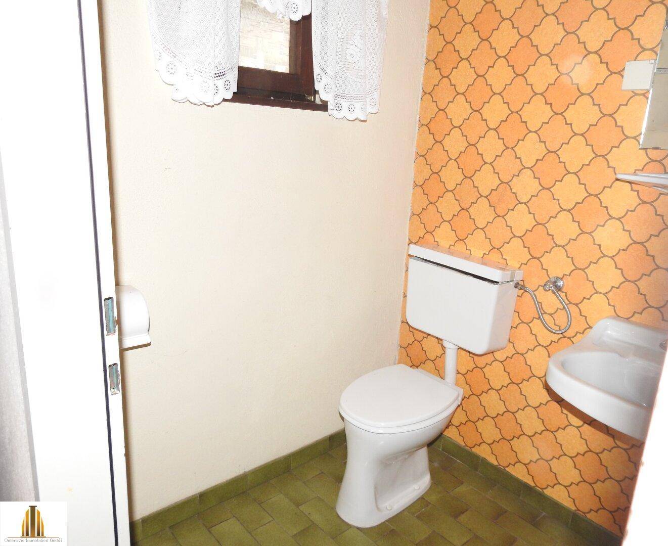 Kleines WC mit Fenster, Waschbecken und auffälliger orangefarbener Tapete.
