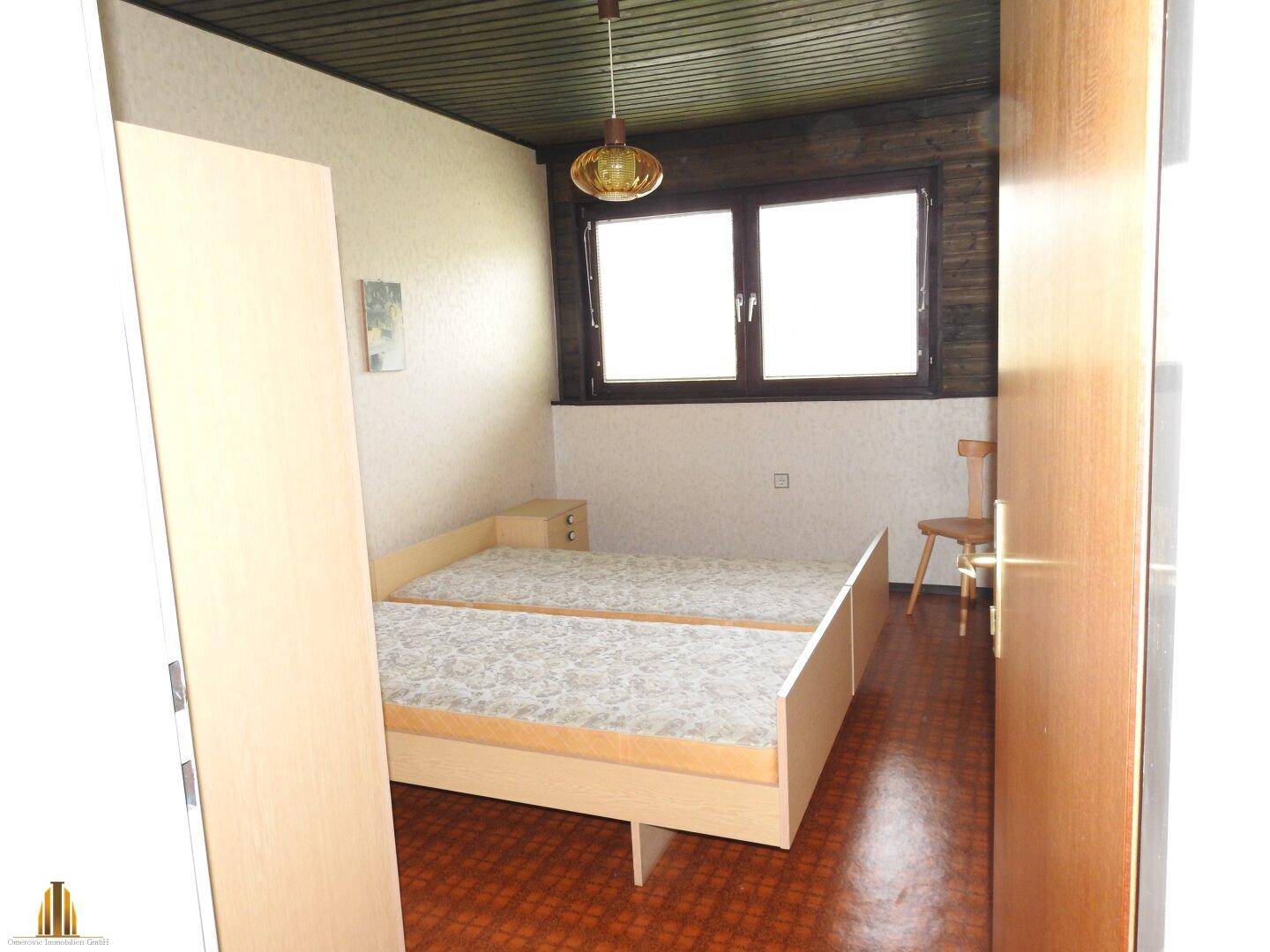 Schlafzimmer mit zwei Einzelbetten, Holzdecke und Fenster in einfacher Ausstattung.