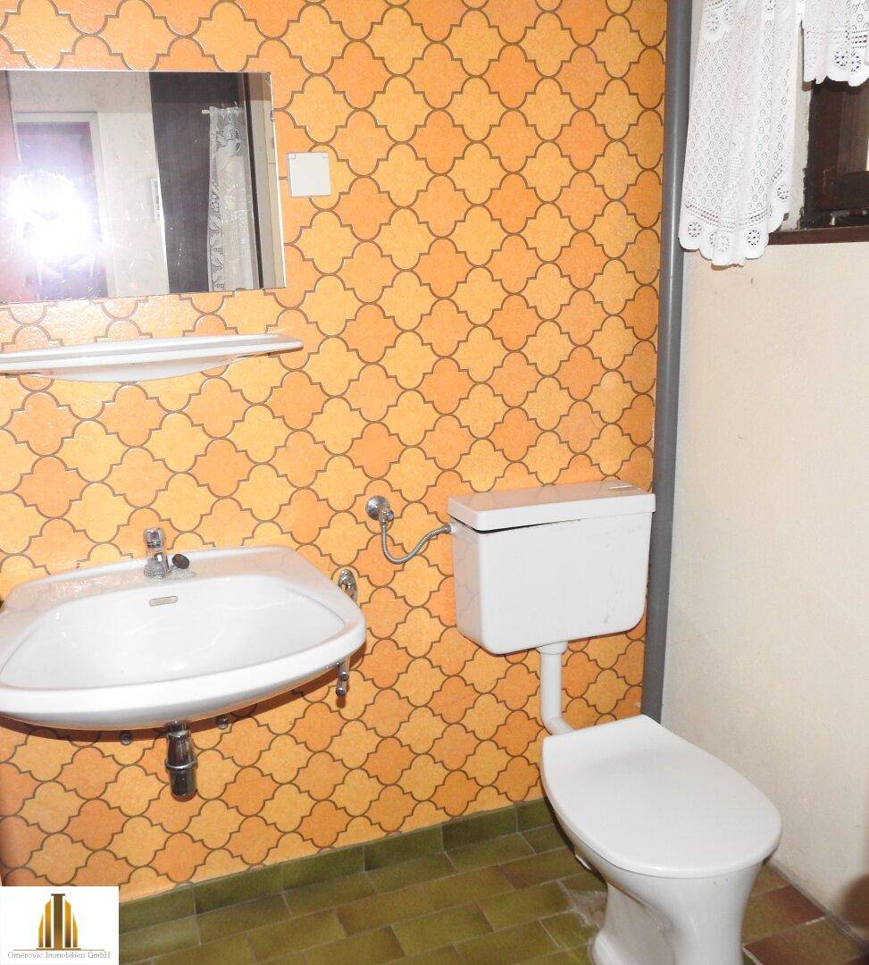 Kleines WC mit Waschbecken, Toilette und auffälligen Retro-Fliesen im 80er-Jahre-Stil.