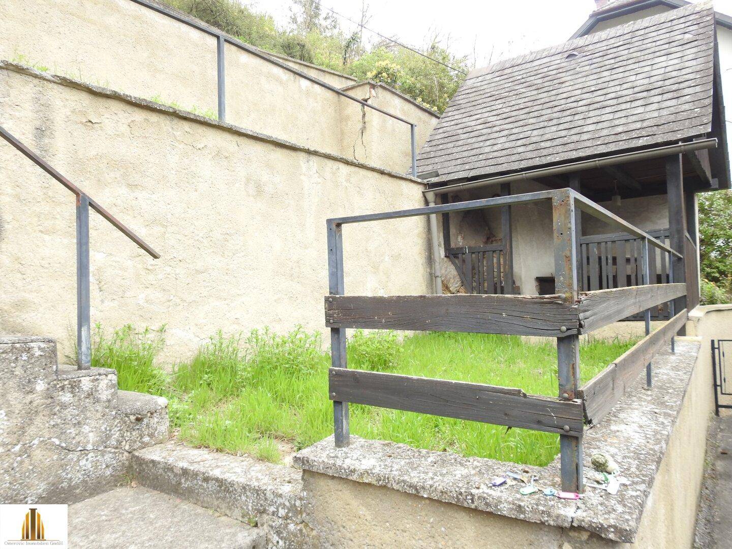 Außenbereich mit Treppe, alter Mauer und kleiner Rasenfläche am Hang gelegen.