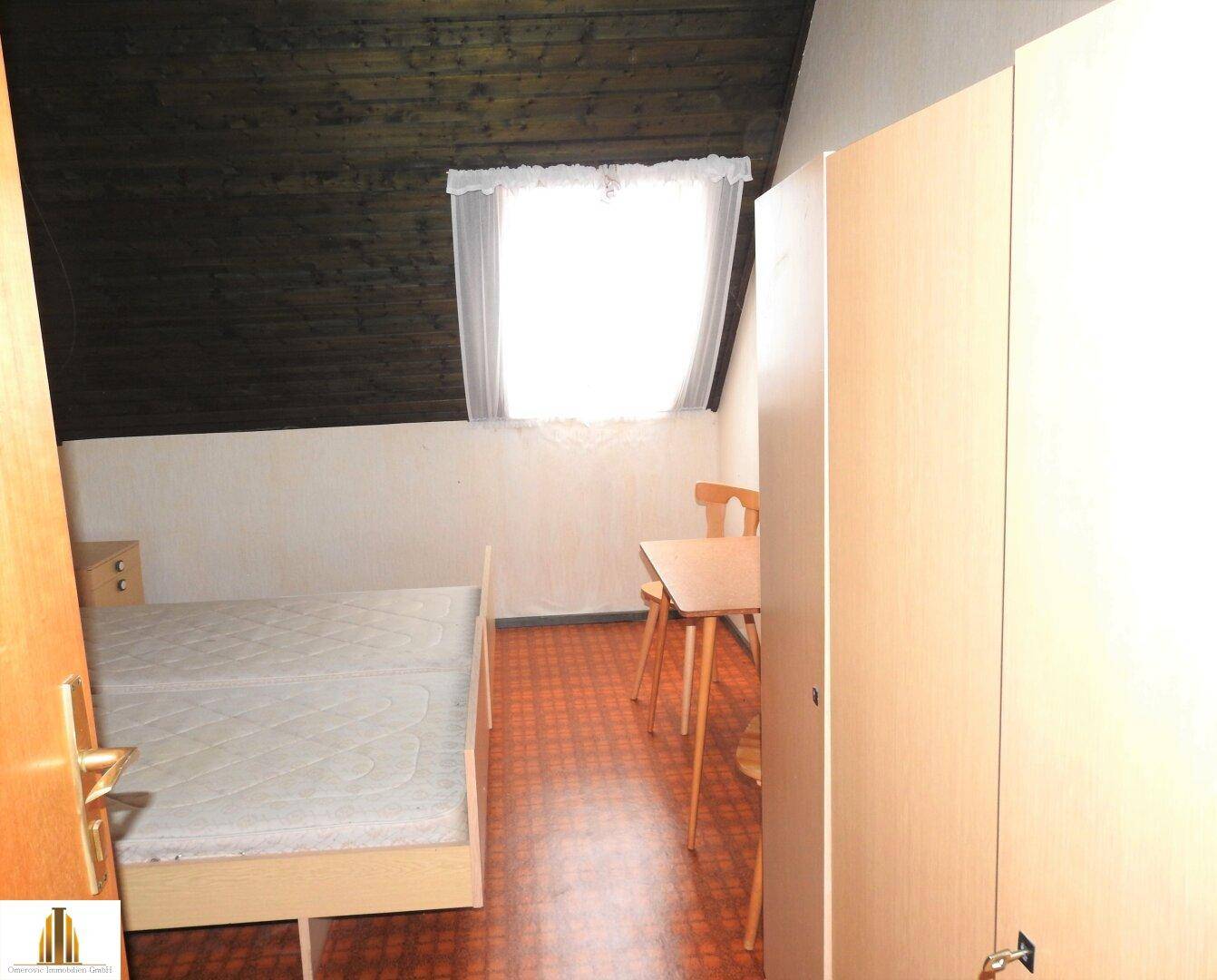 Dachschlafzimmer mit schräger Decke, Fenster und Holzverkleidung, typisch für den Dachboden.