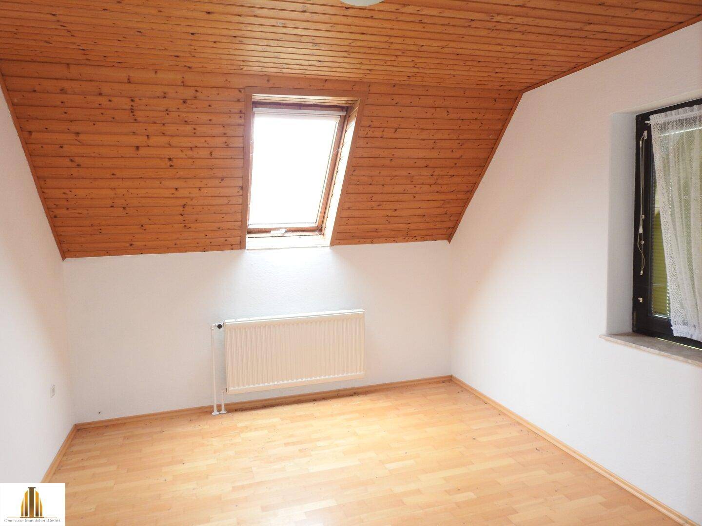Helles Schlafzimmer im Dachgeschoss mit Holzdecke, Dachfenster und Laminatboden.