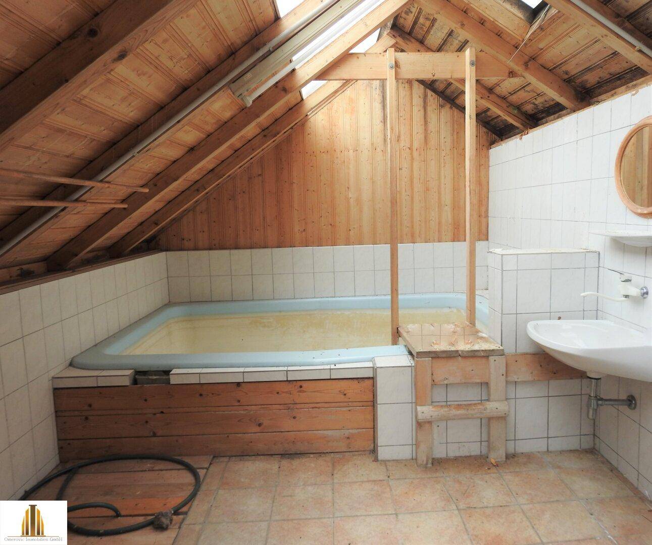 Badezimmer im Dachgeschoss mit großer Badewanne, Holzverkleidung und Dachfenster.