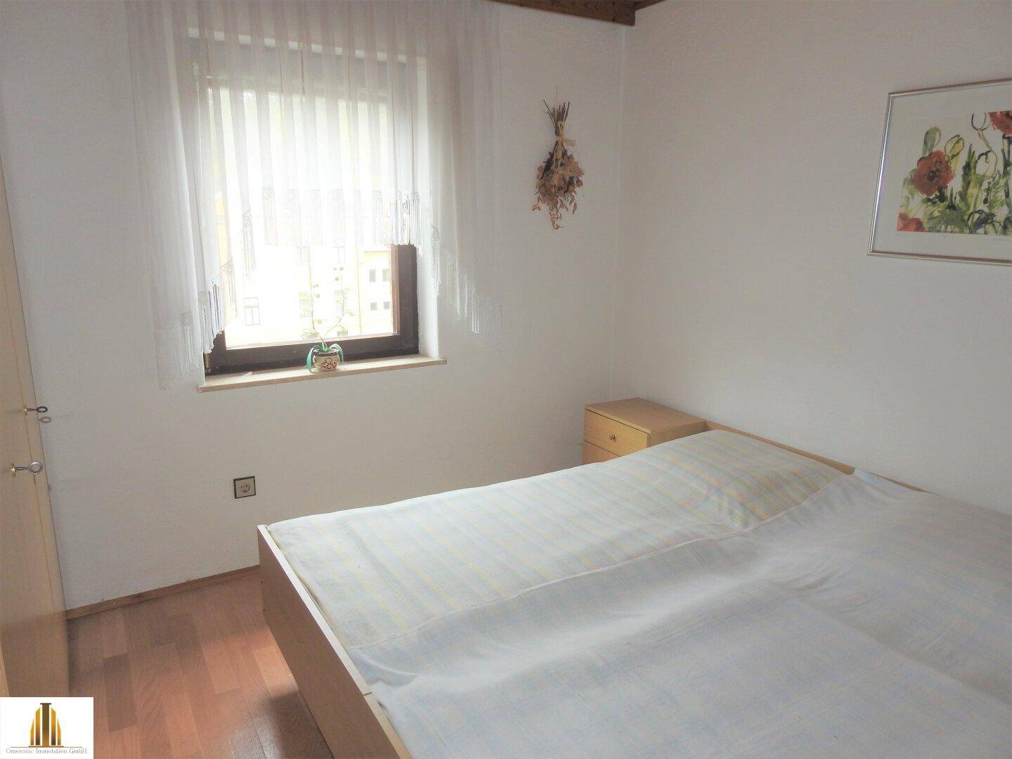 Schlafzimmer mit Doppelbett, Nachttisch und hellem Fenster, gemütlich eingerichtet.