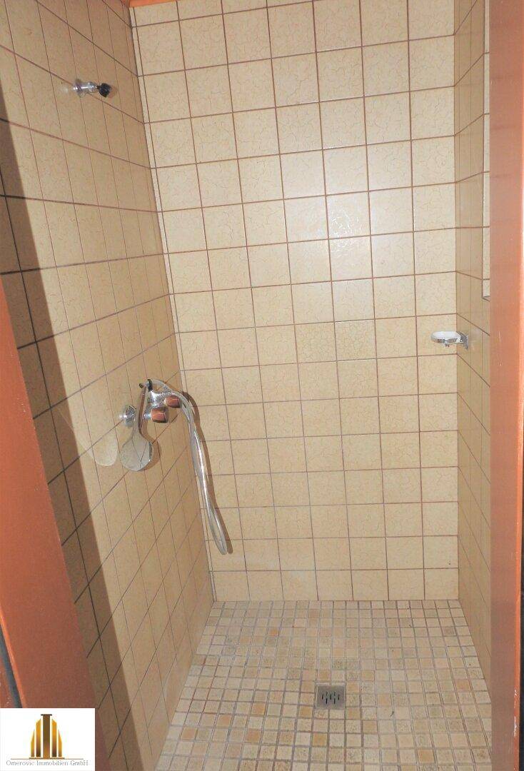 Geflieste Duschkabine mit beigen Fliesen und einfacher Ausstattung, funktional und sauber.