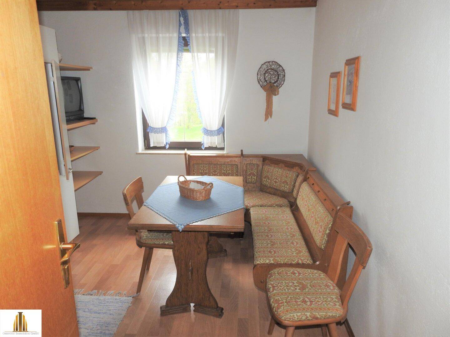 Essbereich mit Eckbank, Holztisch und Fenster mit Vorhängen, traditionell eingerichtet.