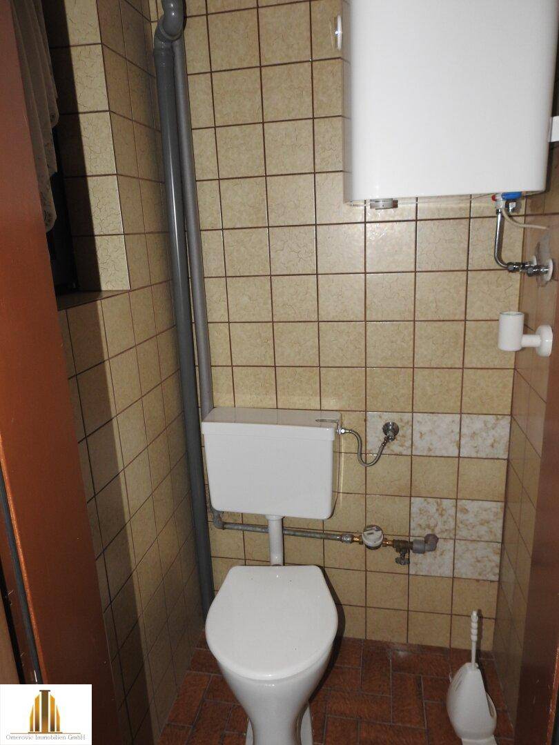 Kleines WC mit Toilette, Boiler und beigen Wandfliesen, einfach und sauber.