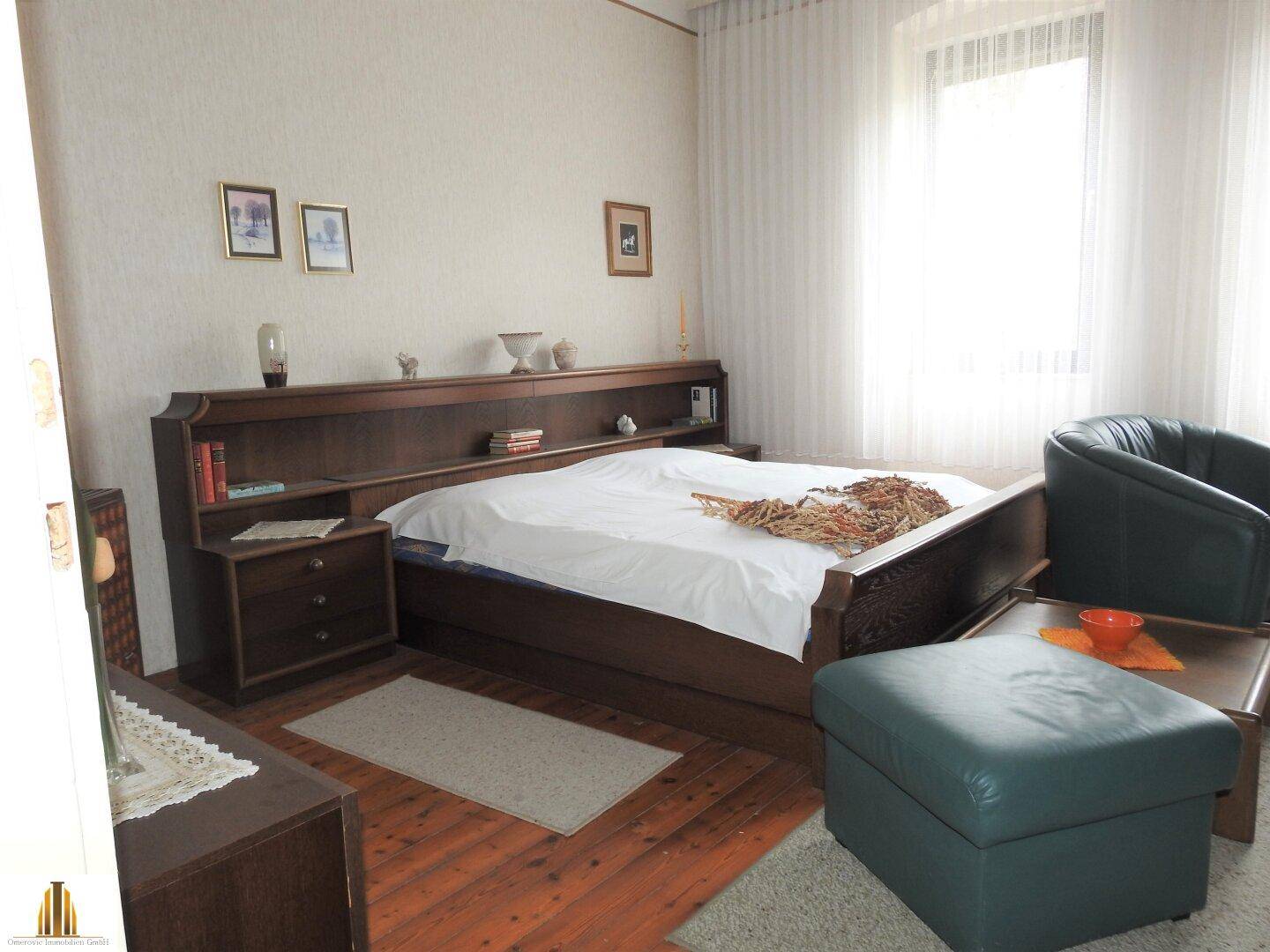 Geräumiges Schlafzimmer mit großem Bett, Sessel und Ofen, hell und einladend.