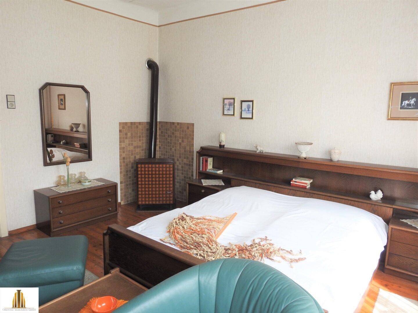 Schlafzimmer mit Doppelbett, Kaminofen und Sitzgelegenheit, traditionell eingerichtet.