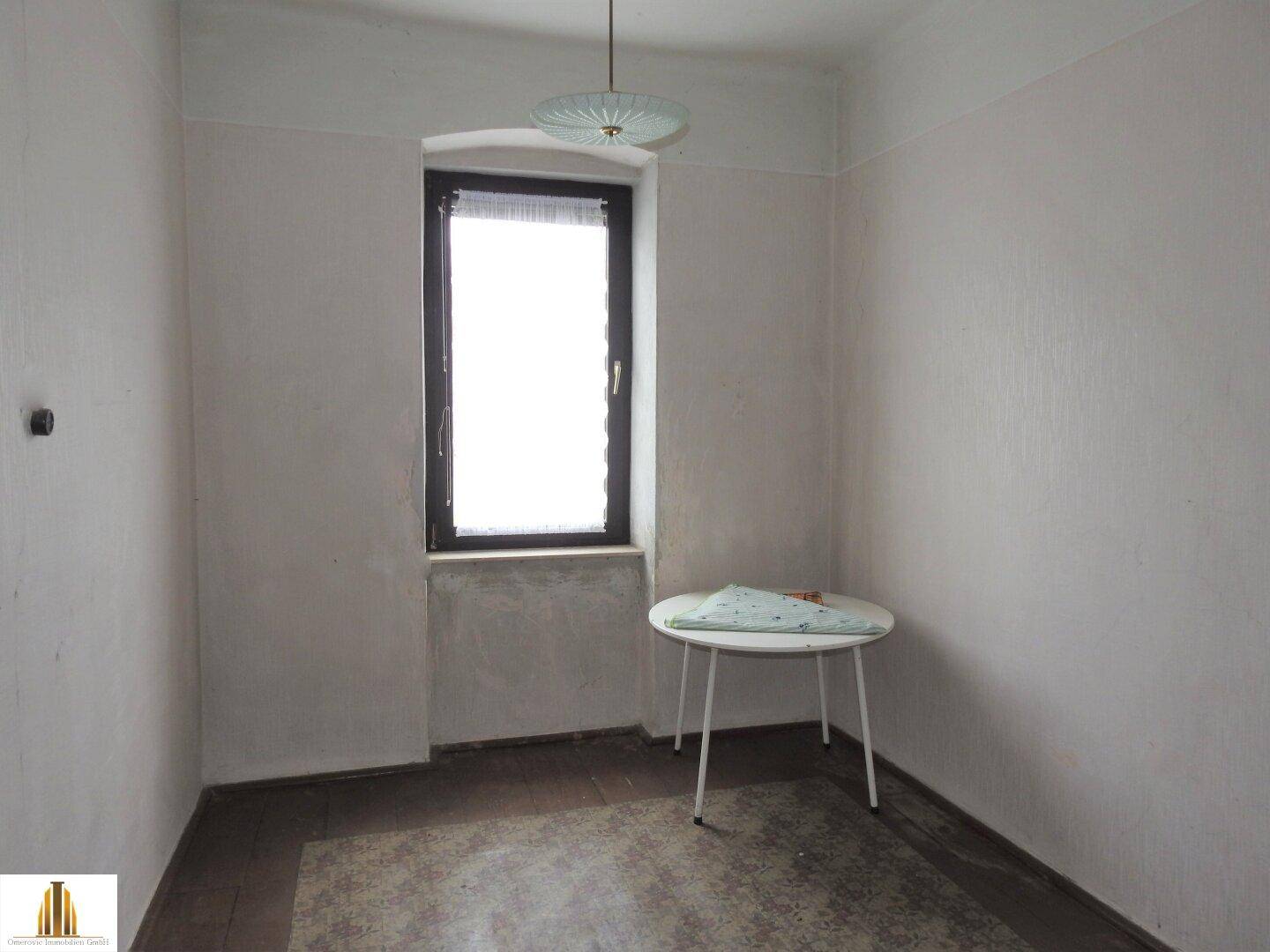 Kleiner Raum mit Fenster, Tisch und schlichten Wänden, vielseitig nutzbar.