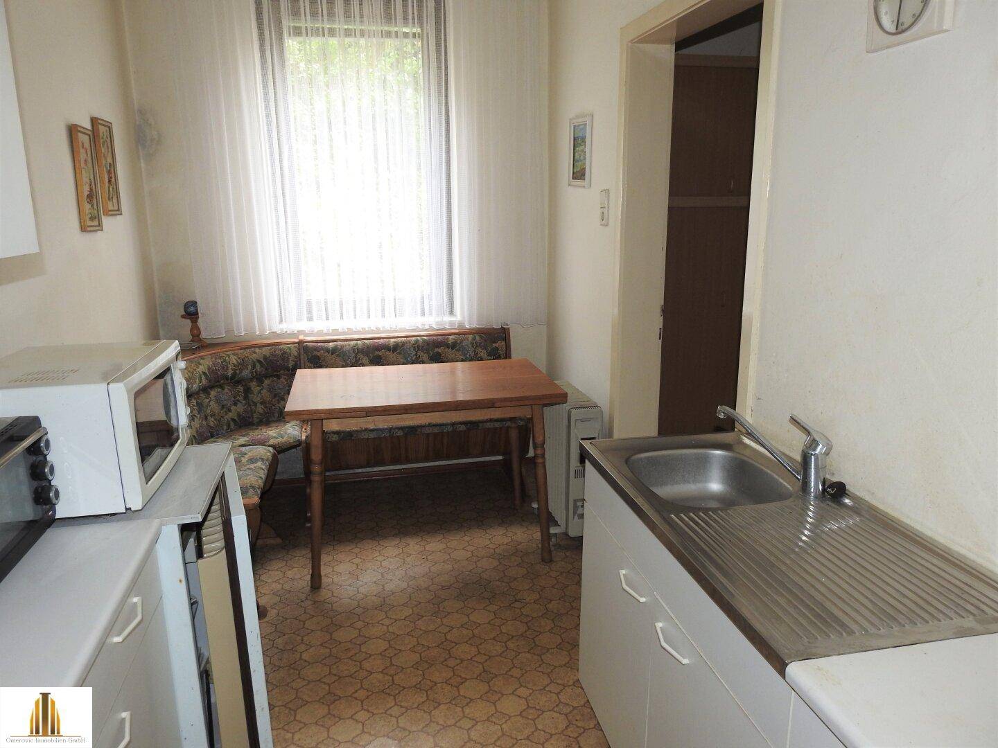 Gemütliche Küche mit Essbereich, Spüle und Blick ins Grüne durch das Fenster.