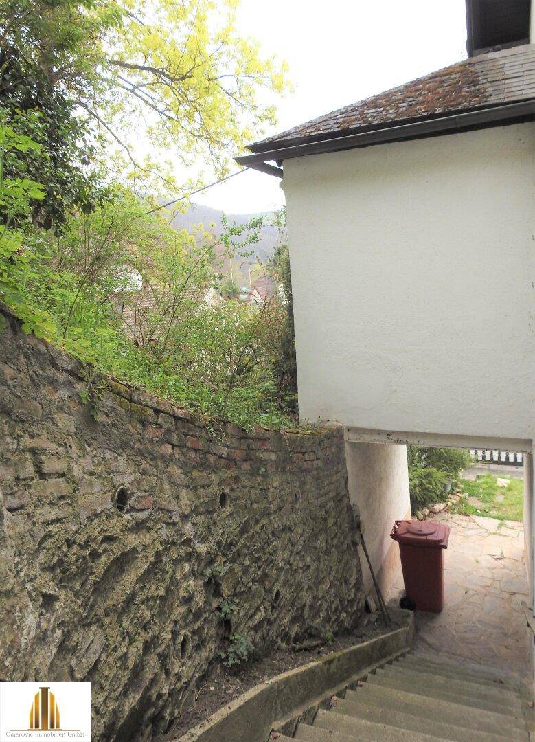 Außentreppe führt entlang einer alten Steinmauer zu einem Eingangsbereich.