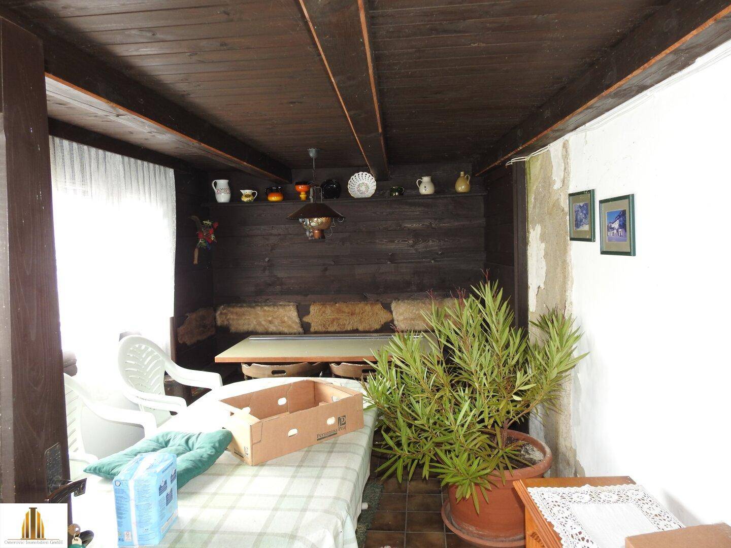 Überdachter Außenbereich mit Holzbalkendecke, Sitzgelegenheiten und Pflanzen.