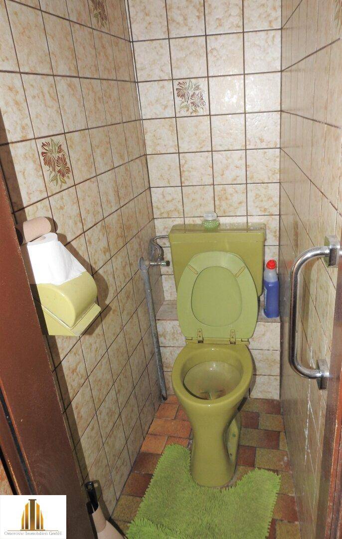 Separate Toilette mit grüner Keramik und passenden Fliesen.