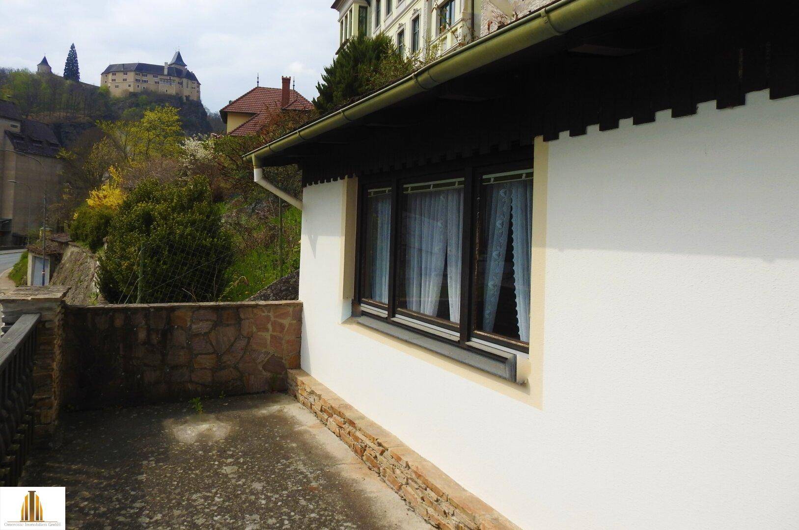 Terrasse mit Steinmauer und Blick auf die umliegende Landschaft und eine Burg.