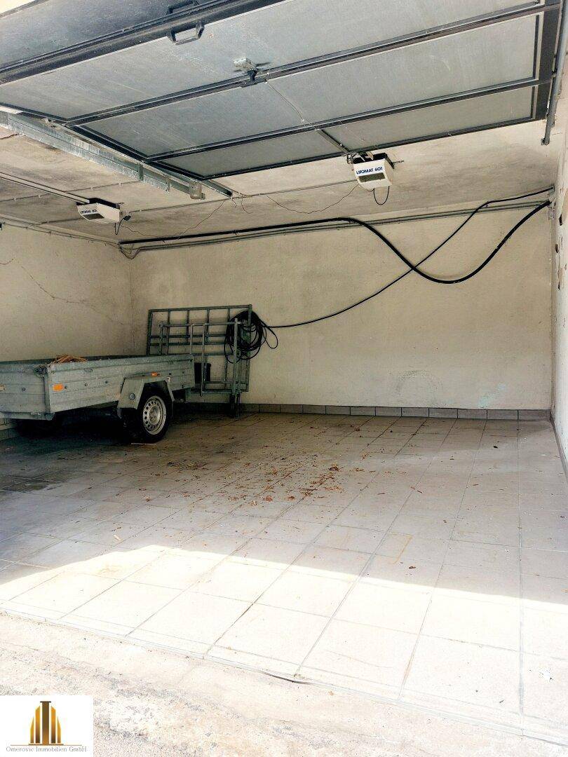 Geräumige Garage mit gefliestem Boden und einem Anhänger, bereit zur Nutzung.
