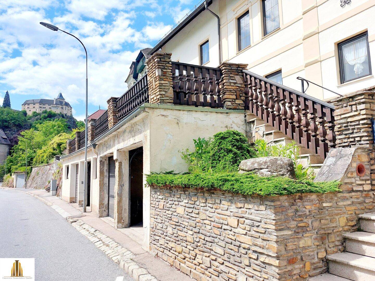 Seitenansicht eines Gebäudes mit Steinfassade, Außentreppe und Blick auf eine Burg.