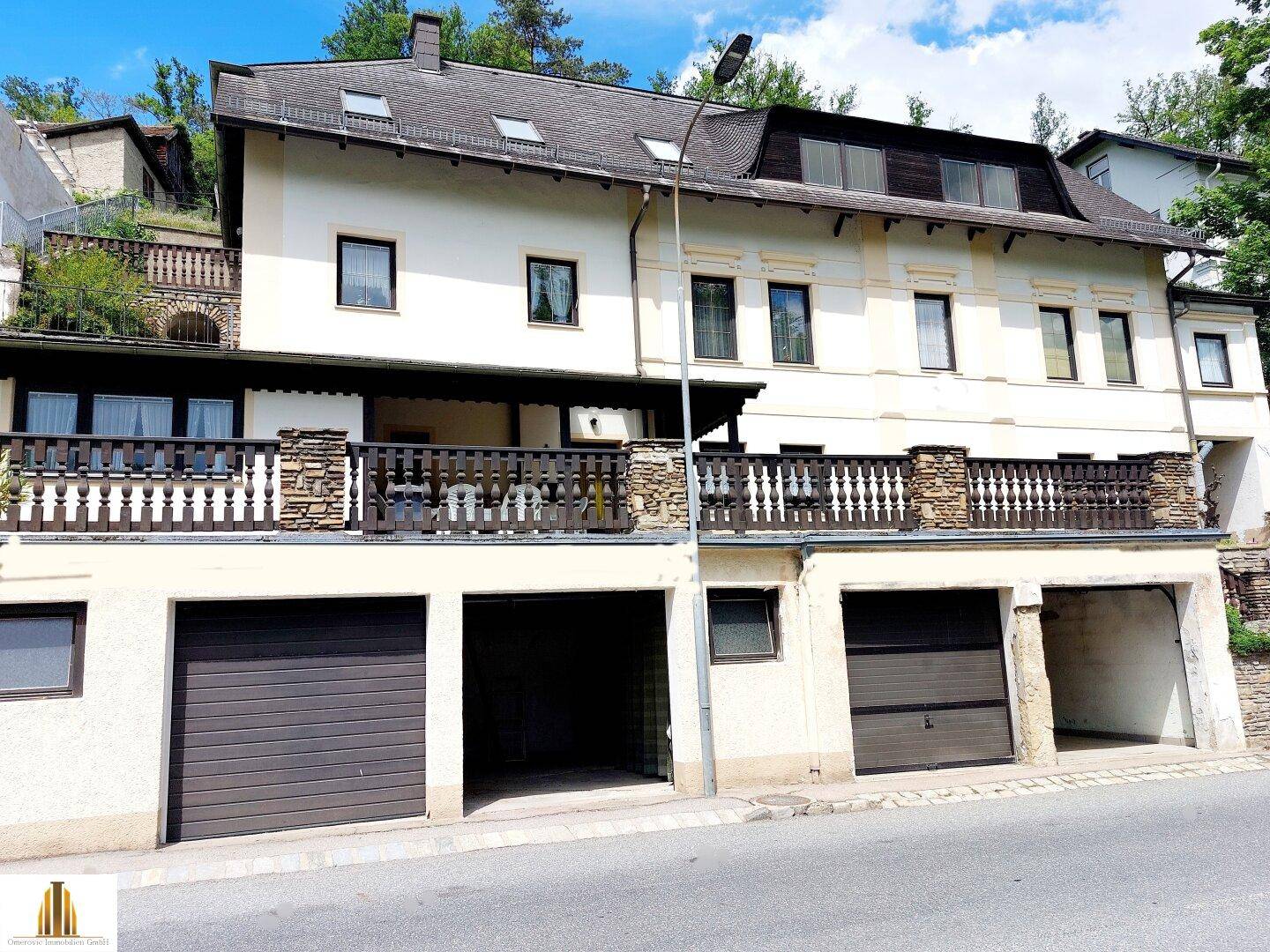 Vorderansicht des Gebäudes mit zwei Garagen und einem Balkon im oberen Bereich.