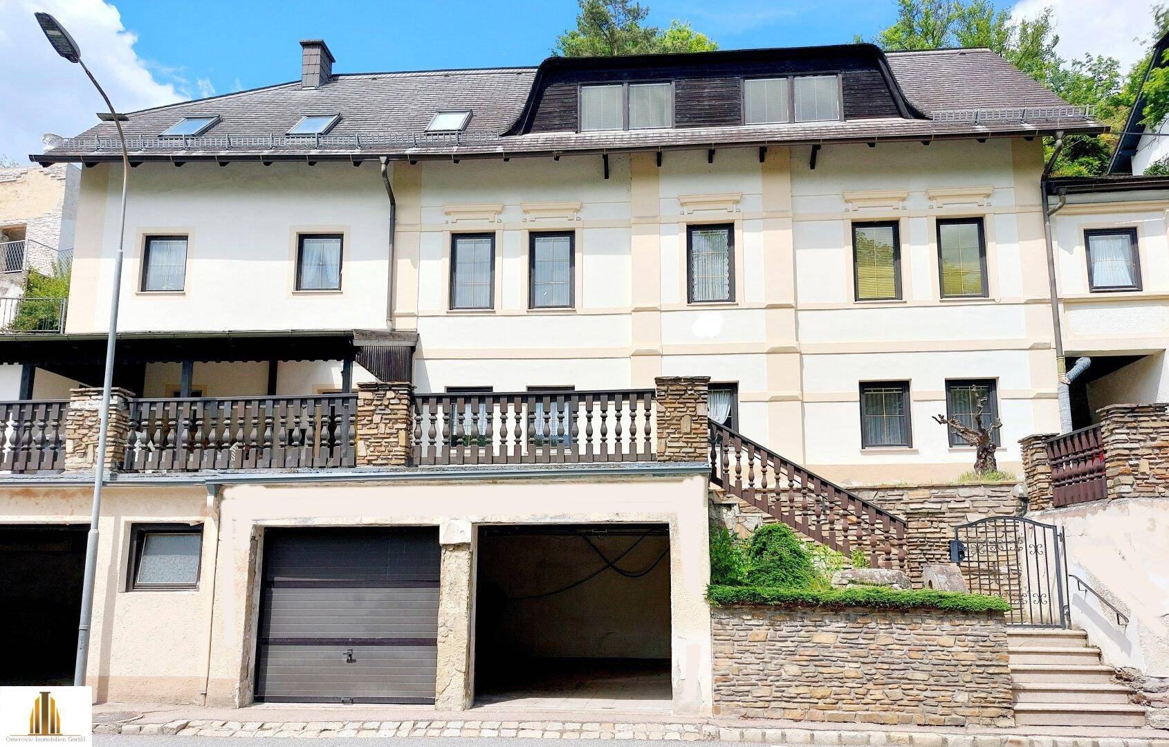 Mehrstöckiges Gebäude mit Garagen im Erdgeschoss und Balkonen, umgeben von Grün.