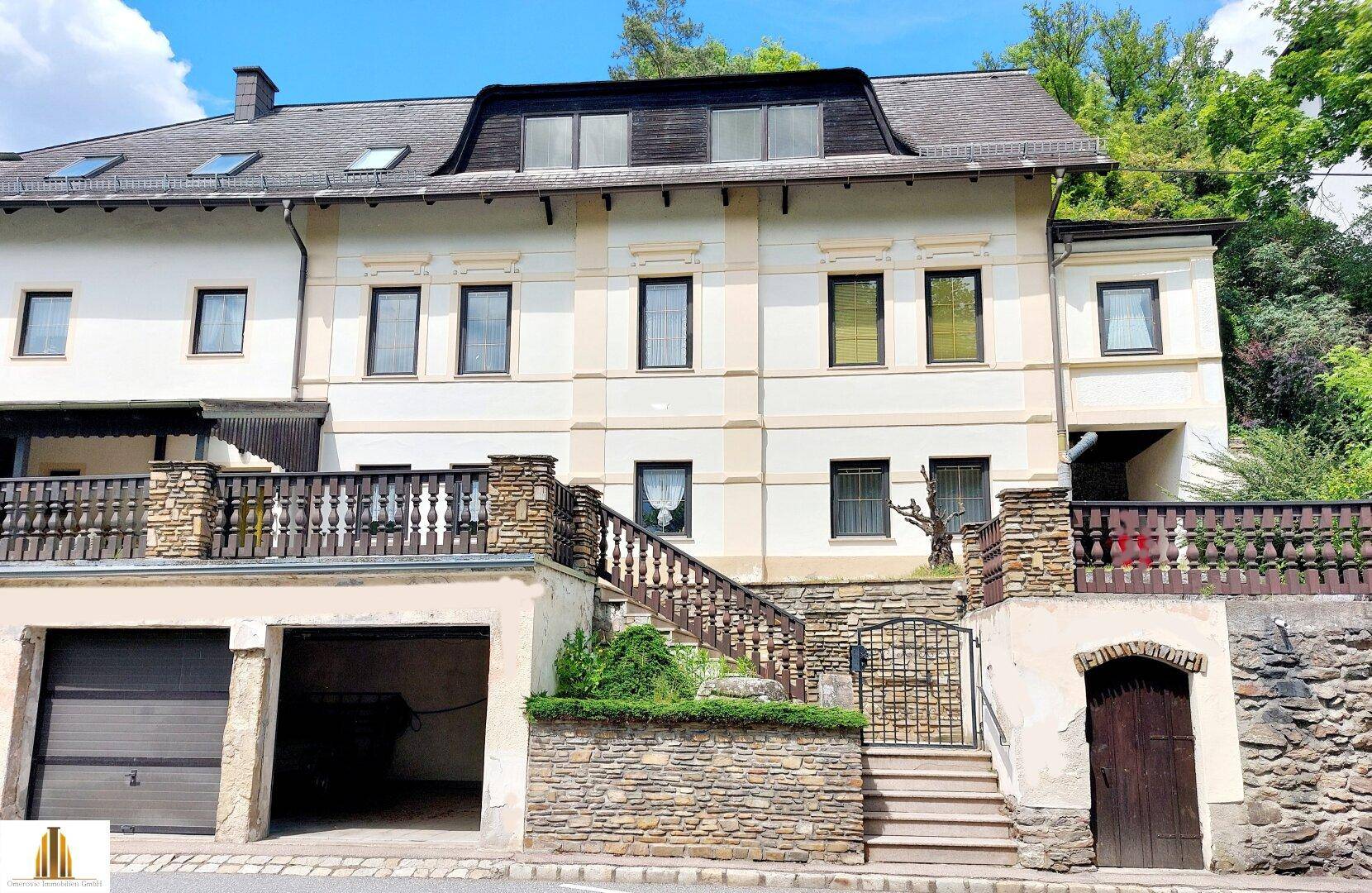 Ansicht des Mehrfamilienhauses mit Steintreppe, schmiedeeisernem Tor und Garagen.