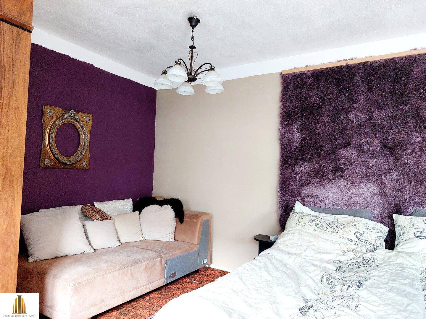 Schlafzimmer mit violetten Wänden, einem Sofa und einem Bett mit flauschigem Kopfteil.