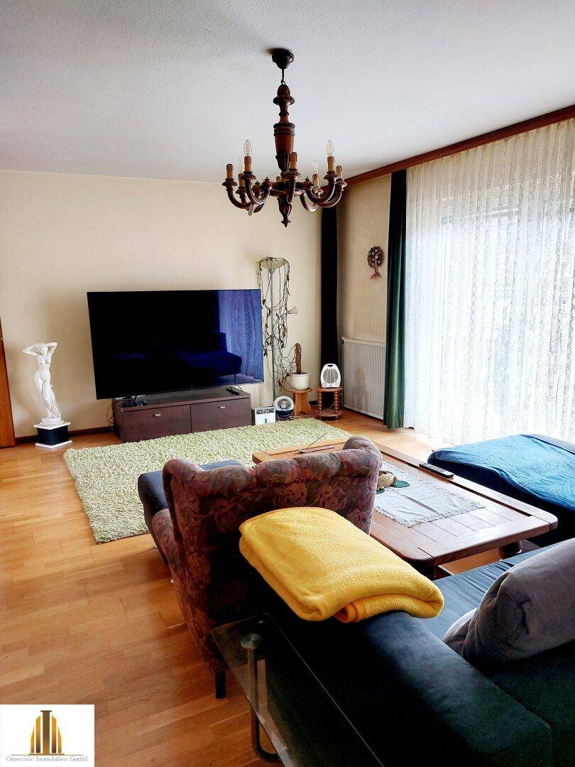 Gemütliches Wohnzimmer mit Parkettboden, großem Fernseher und traditionellem Kronleuchter.