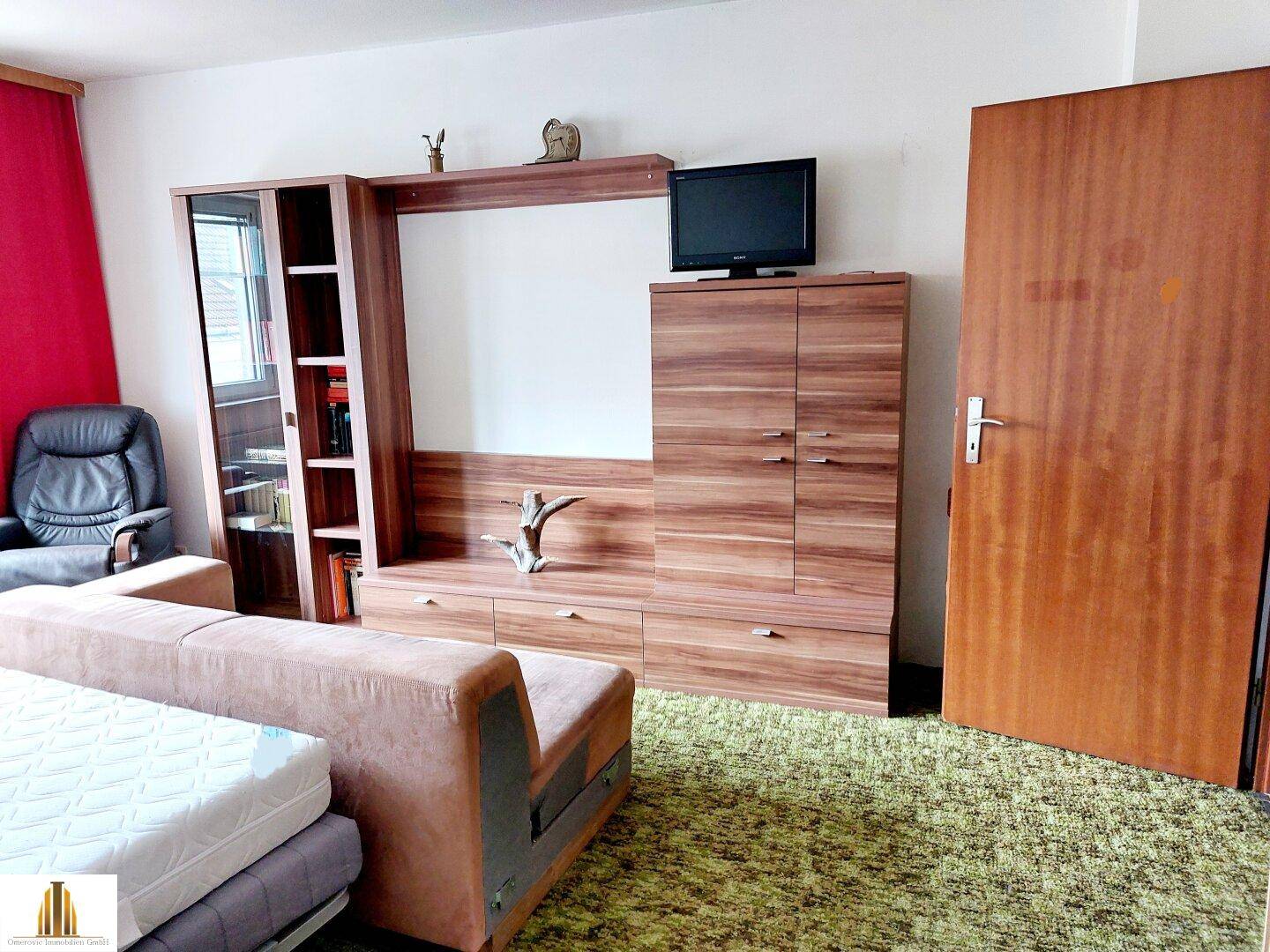 Zimmer mit grünem Teppichboden, großer Schrankwand und einem Sofa.