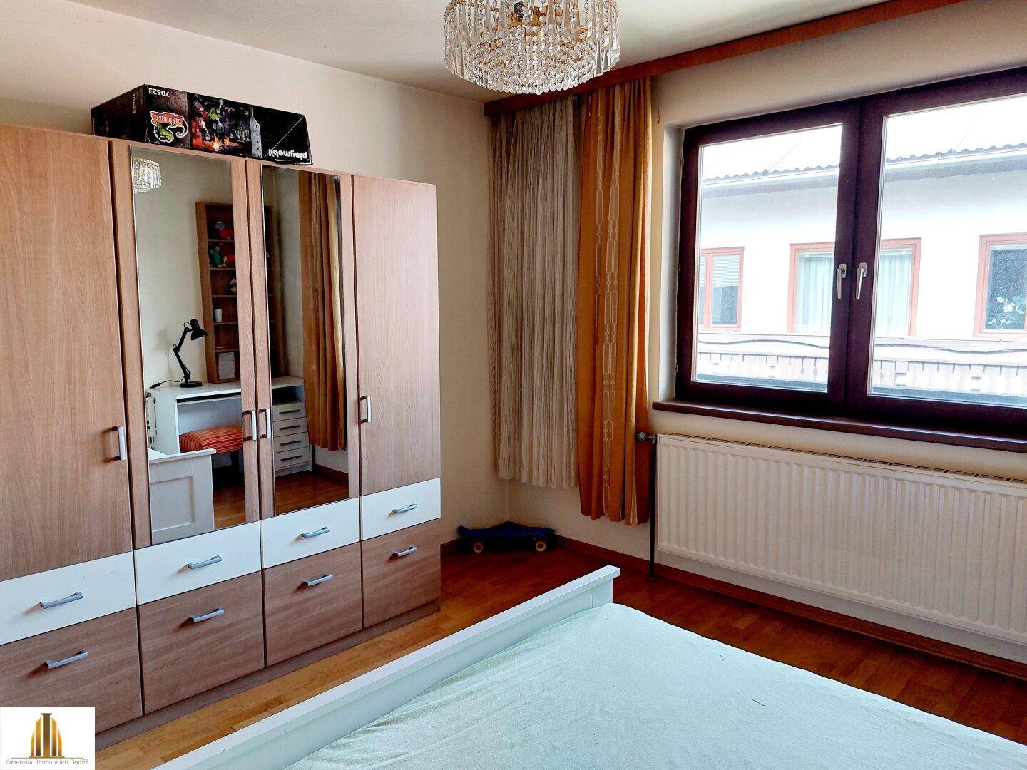 Schlafzimmer mit Holzboden, großem Kleiderschrank und Fenster mit Vorhängen.