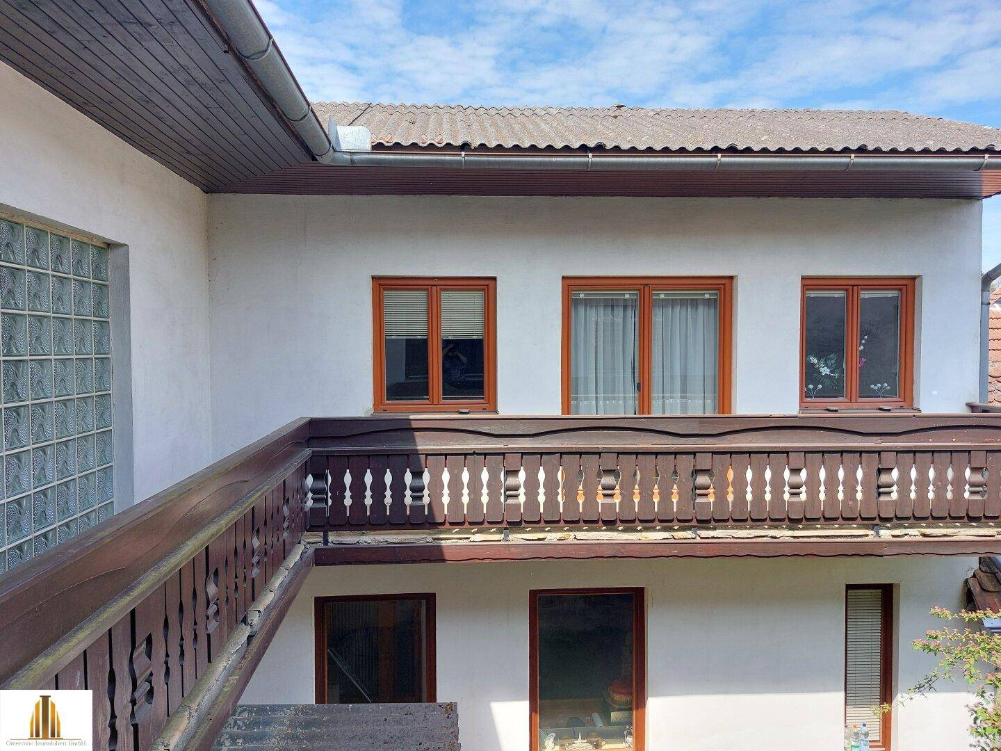 Blick auf die Hausfassade mit einem traditionellen Holzbalkon und Fenstern im Obergeschoss.