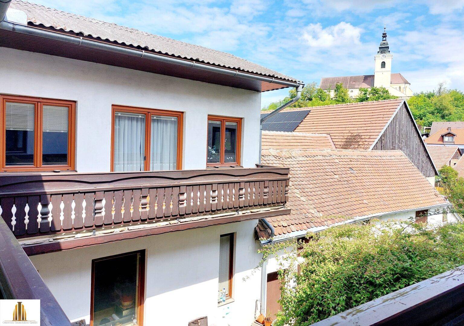 Balkon mit traditionellem Holzgeländer und Blick auf die Dächer der Nachbarschaft und eine Kirche.