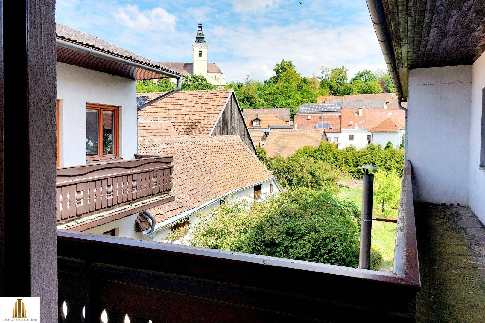 Aussicht vom Balkon über die umliegenden Häuser und die malerische Landschaft mit Kirchturm.