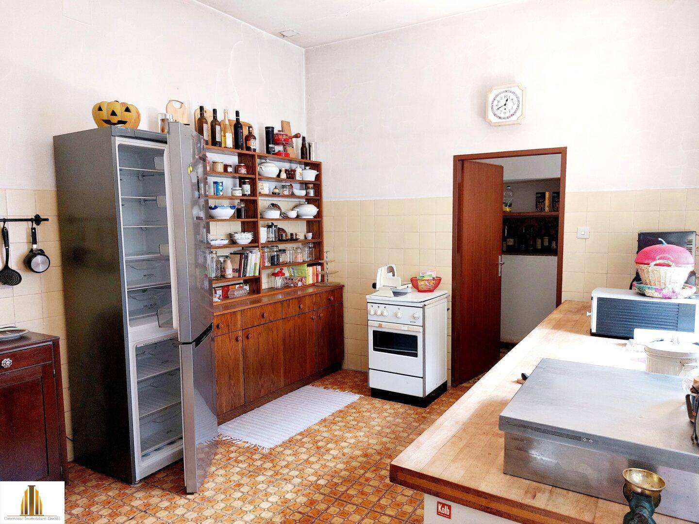 Geräumige Küche mit älteren Fliesen, freistehendem Kühlschrank und einfacher Ausstattung.
