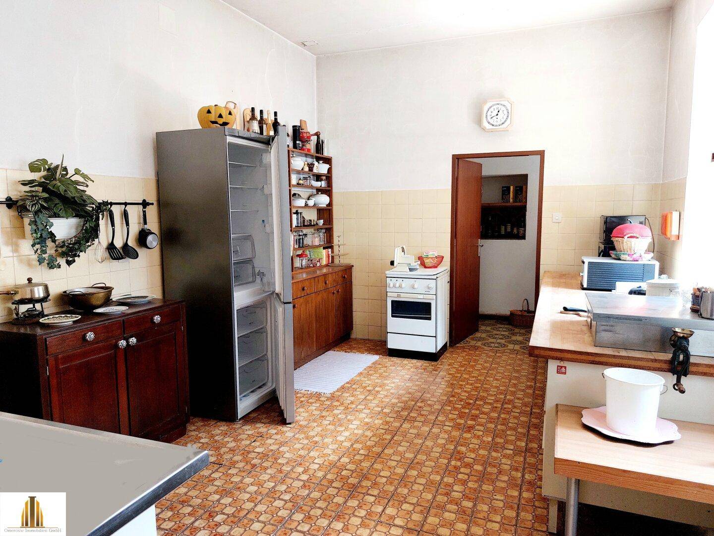 Geräumige Küche mit älteren Fliesen, freistehendem Kühlschrank und einfacher Ausstattung.