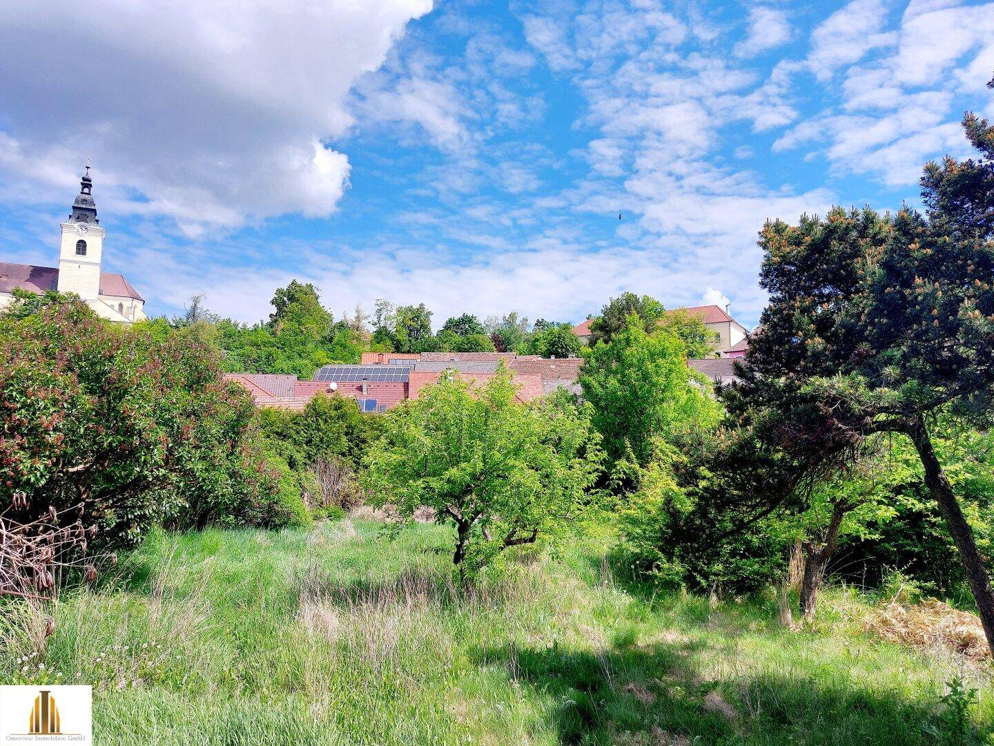 Großer Garten mit Bäumen und Blick auf die Dächer der Ortschaft und die Kirchturmspitze.