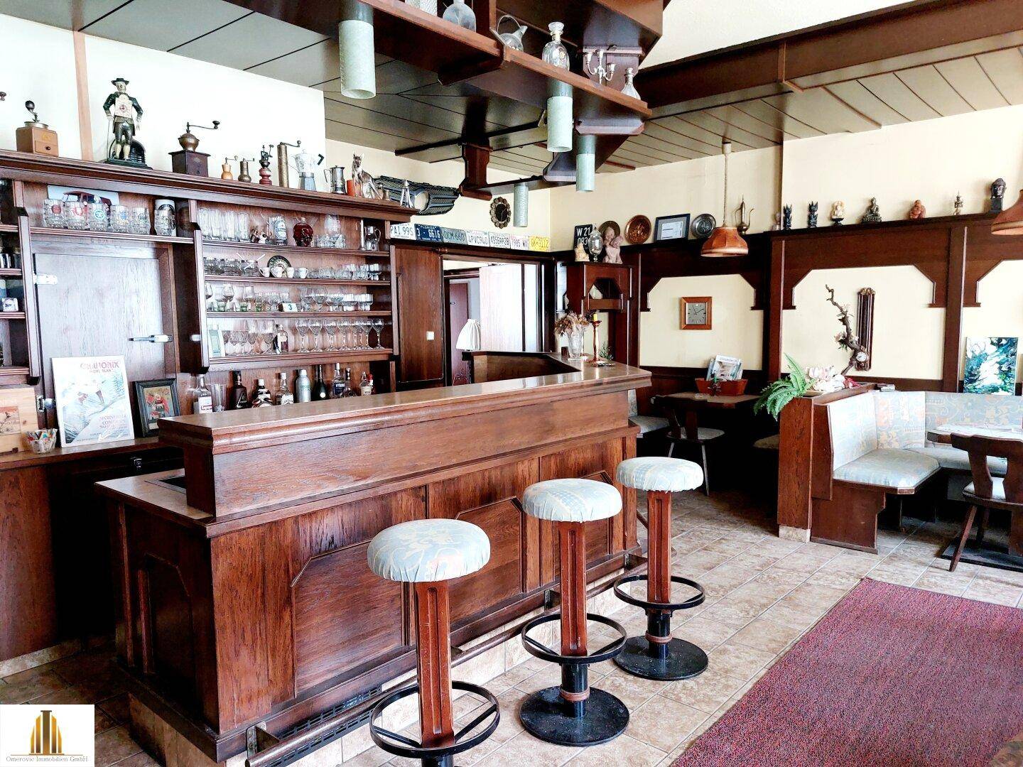 Traditionelle Holzbar mit Barhockern und gefliestem Boden, umgeben von rustikalen Möbeln.