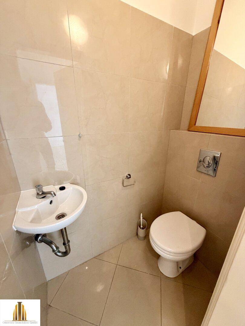 Kleines Gäste-WC mit Wand-WC, Eckwaschbecken und beigefarbenen Fliesen.