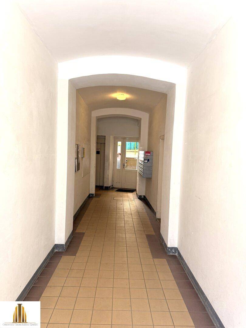 Langer, gefliester Flur mit gewölbter Decke und Eingangstür am Ende.