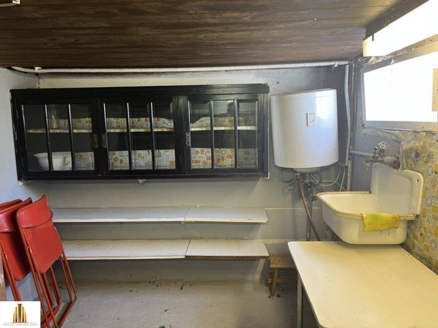Hauswirtschaftsraum im Keller mit Waschbecken, Boiler und Regalen.