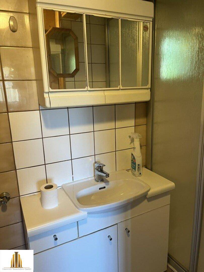 Badezimmer mit Waschbecken, Spiegelschrank und weißen Fliesen in Standardausstattung.
