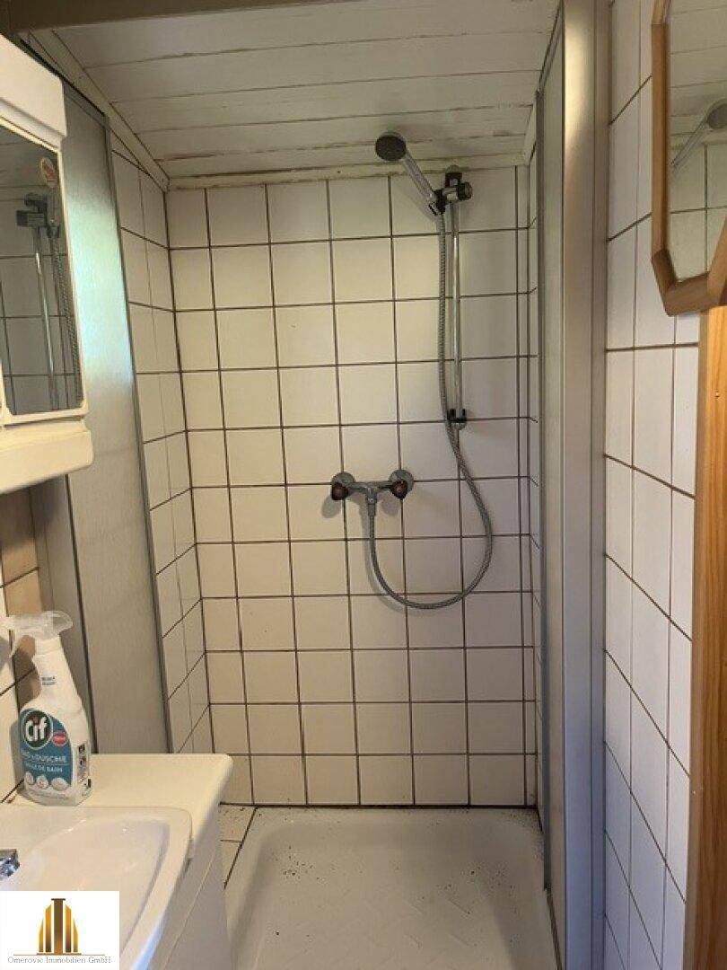 Duschbereich im Badezimmer mit weißen Fliesen und einfacher Duscharmatur.