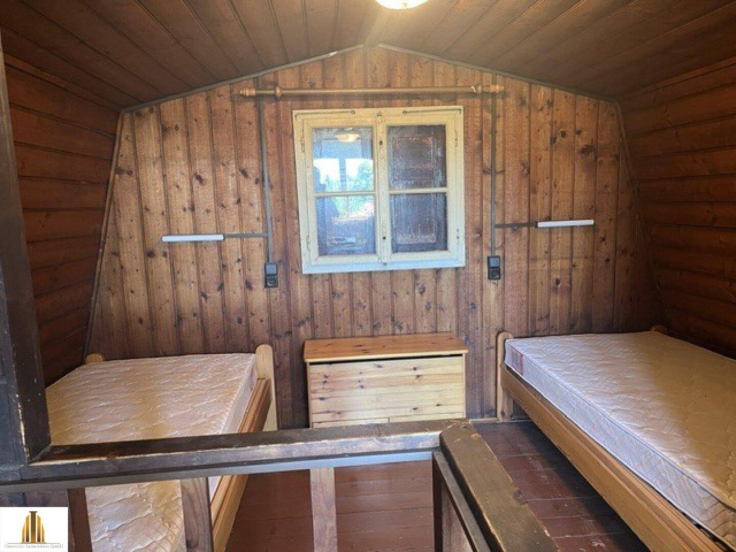 Dachgeschoss-Schlafzimmer mit Holzwänden, zwei Einzelbetten und Dachschräge.
