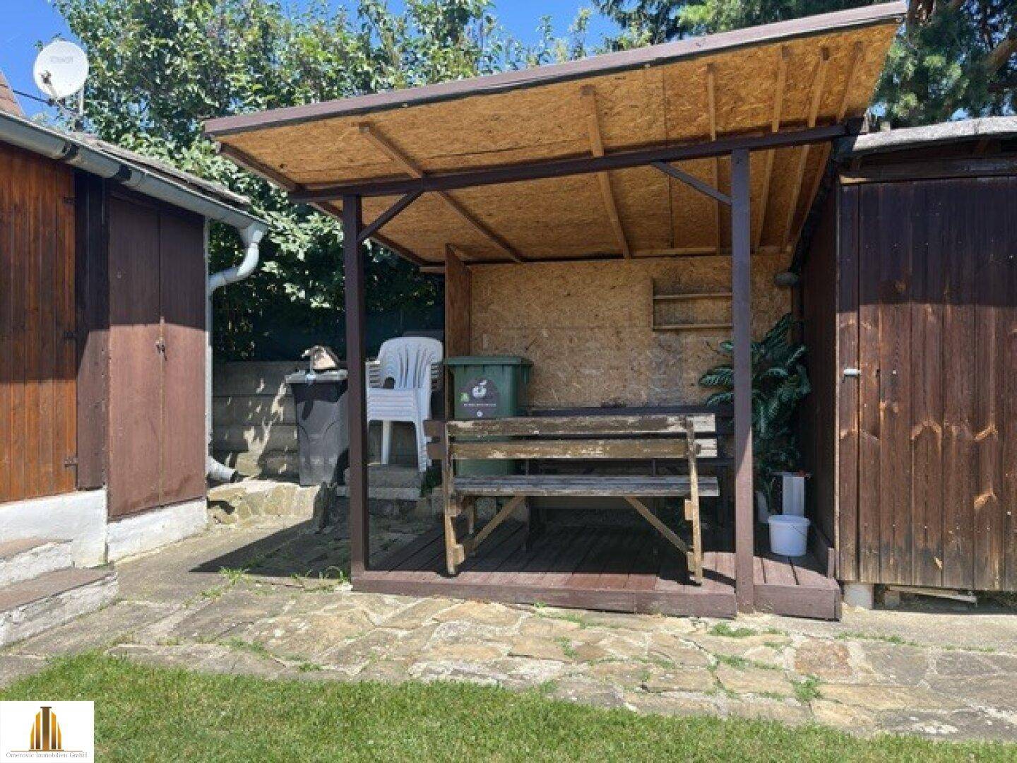 Überdachter Sitzbereich im Freien mit Holzbänken und Blick auf den Garten.