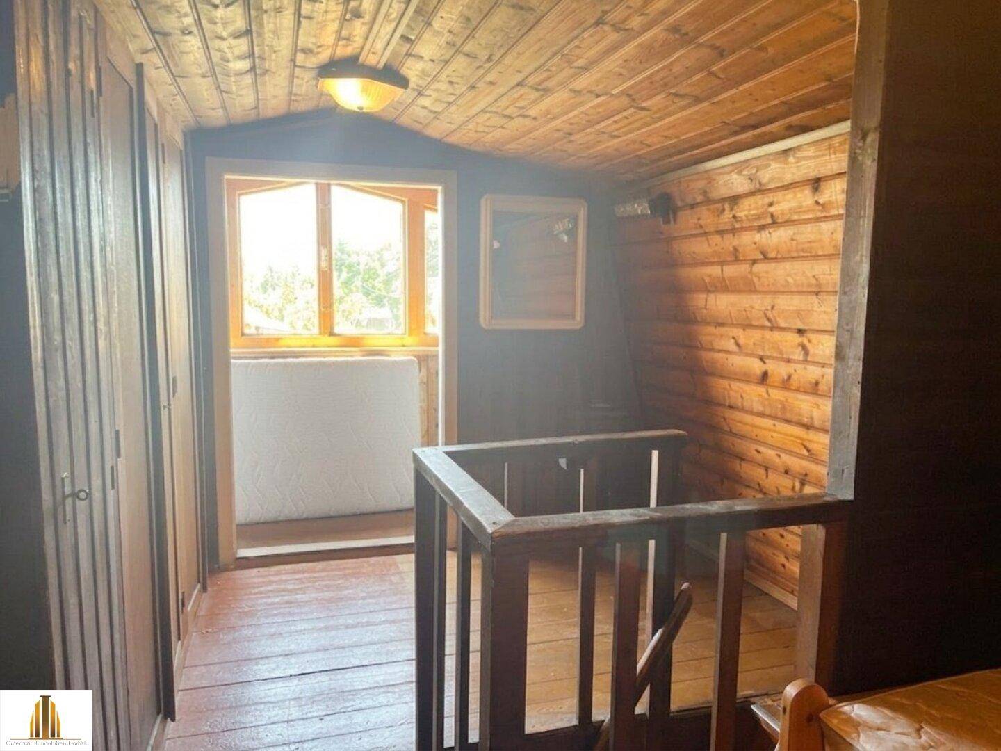 Flur im Obergeschoss mit Holztreppe, Holzboden und Fenster mit Blick nach draußen.