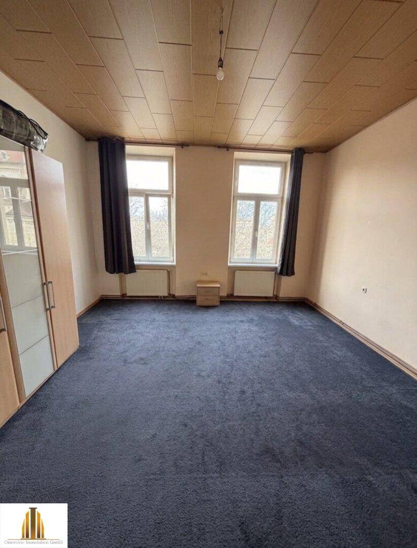 Schlafzimmer mit dunkelblauem Teppichboden, zwei Fenstern und einer Holzdecke.