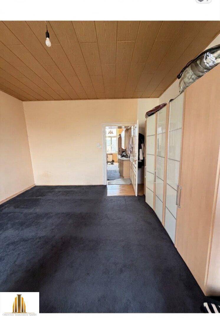 Geräumiges Schlafzimmer mit Teppichboden, Holzdecke und Zugang zu einem weiteren Raum.
