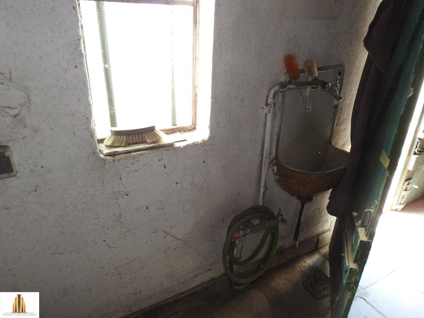 Kleiner Abstellraum mit Fenster, einfachem Waschbecken und Schlauchanschluss.