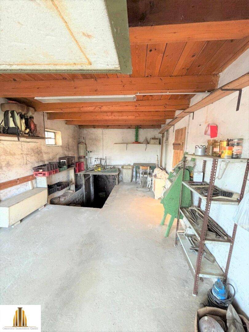 Werkstattähnliche Garage mit Holzbalkendecke, Betonboden und einer Wartungsgrube.