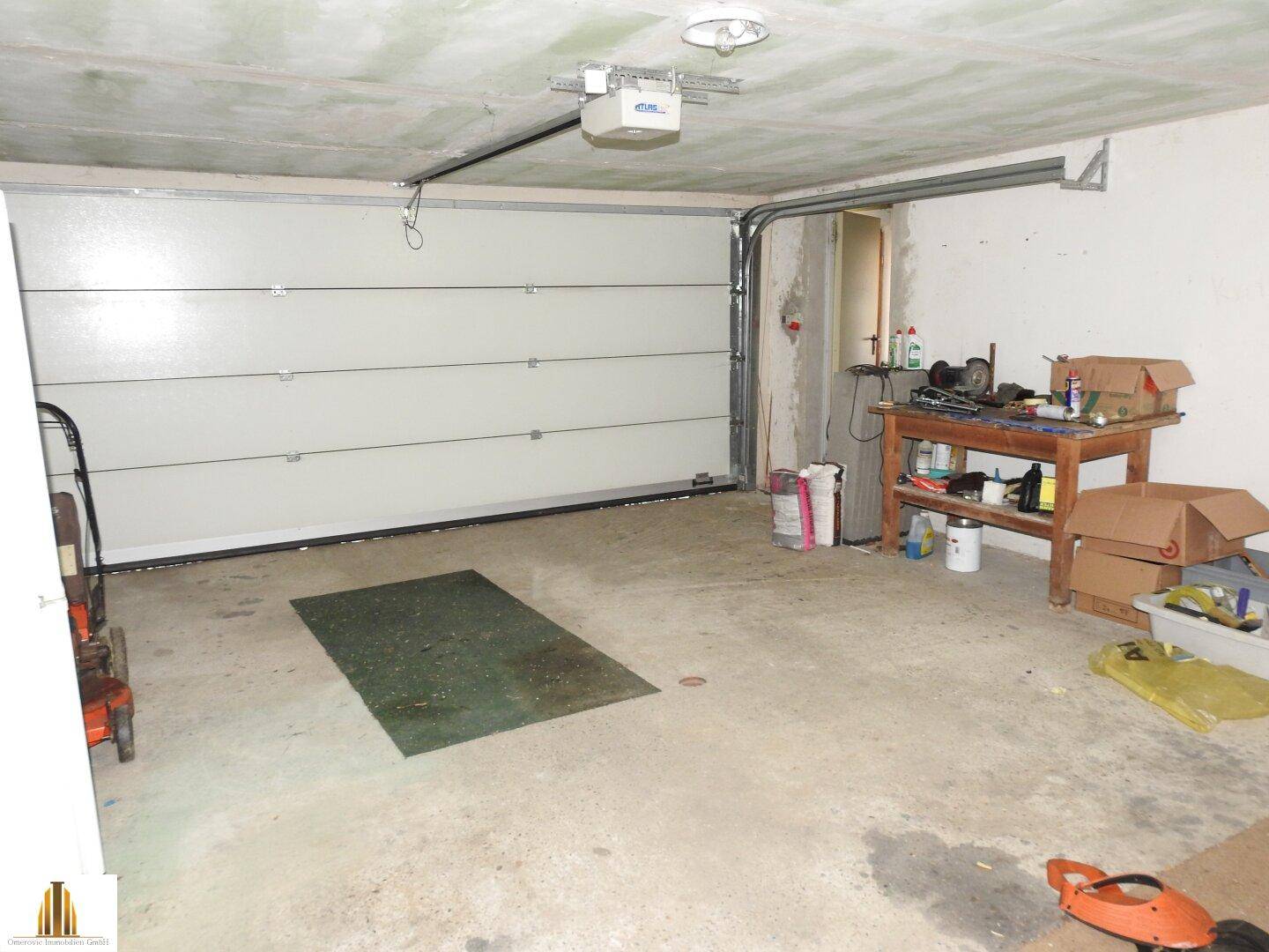 Geräumige Garage mit Betonboden, automatischem Garagentor und Werkbank.